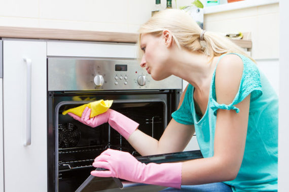 Young woman cleaning oven in the kitchen.