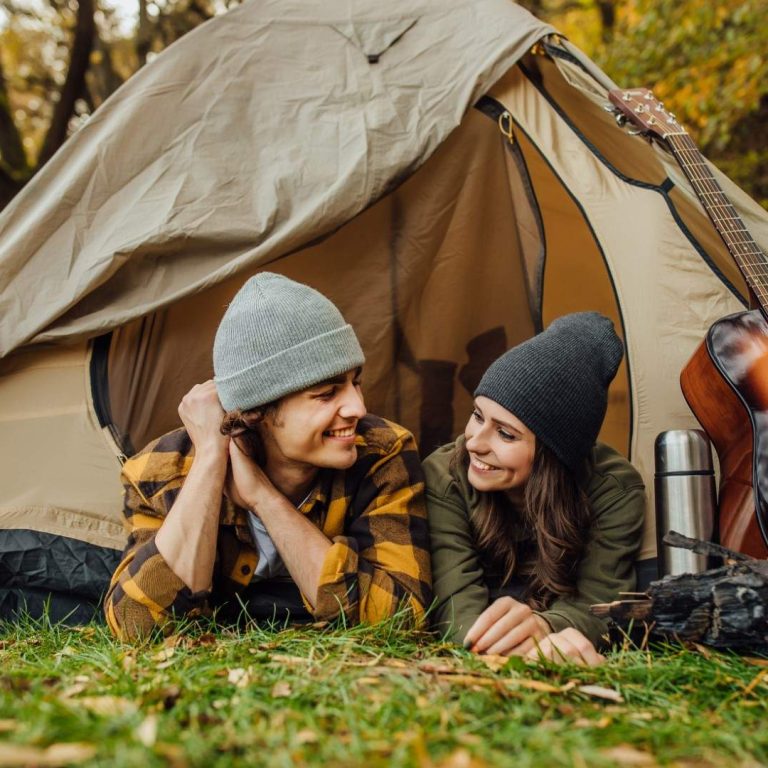 Young loved couple of tourists have a date in the forest. Attractive young woman and handsome man lying in the tent. Hugging lovers near campfire.