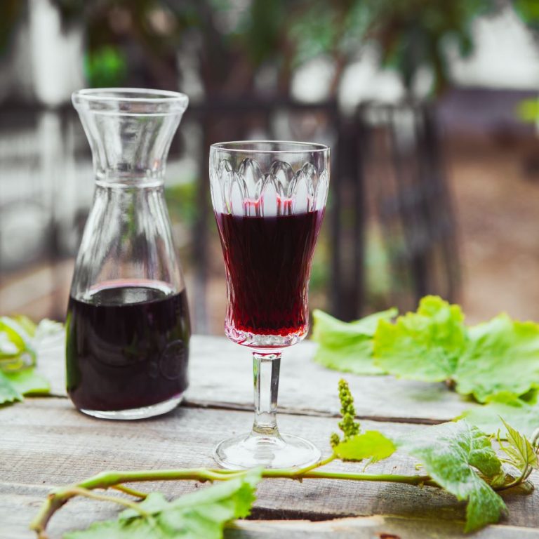 red-wine-jug-glass-with-grape-tree-branch-side-view-wooden-garden-table