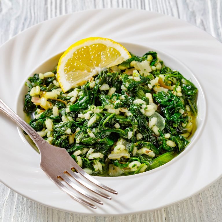 Spanakorizo, Greek spinach and rice pilaf with lemon, dill, spring onion in white bowl with fork on white wooden table, horizontal view from above, close-up