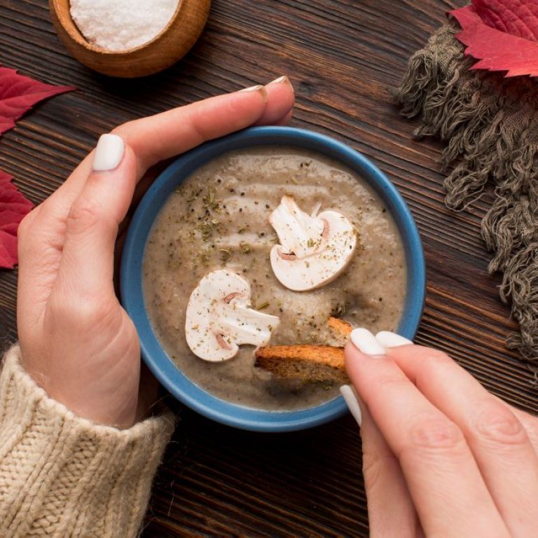 top-view-winter-mushroom-soup-bowl-with-hands-dipping-crouton-it