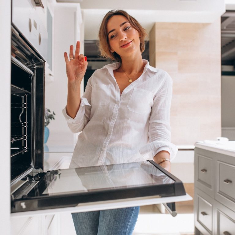 Woman baking at kitchen and looking into the oven